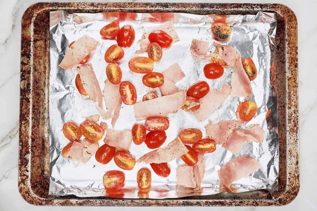 Bacon and halved cherry tomatoes on a baking tray lined with aluminium foil