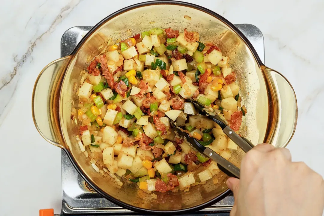 A pot of mixed ingredients being stirred with a cooking thongs