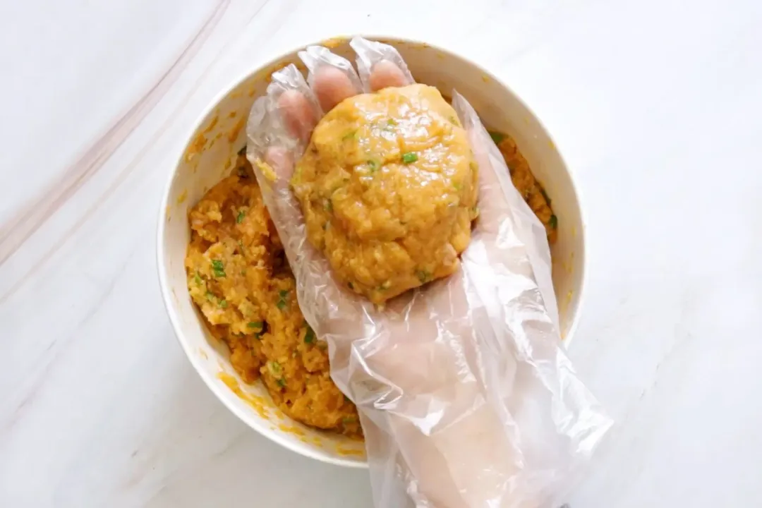 A ball of salmon mixture in the palm of a hand in a plastic glove.