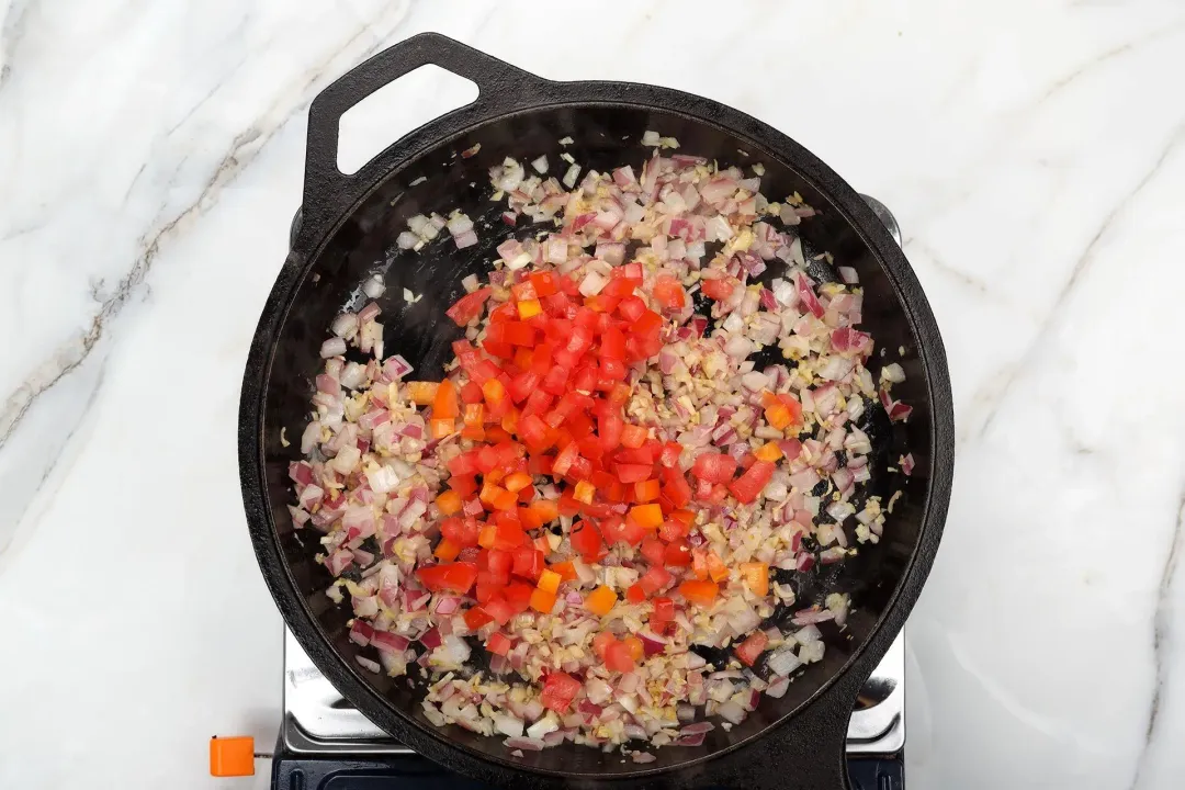 A skillet cooking finely minced aromatics with diced tomatoes and diced carrots