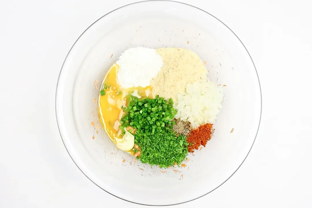 A glass bowl with egg wash, flour, spices, and herbs in it.