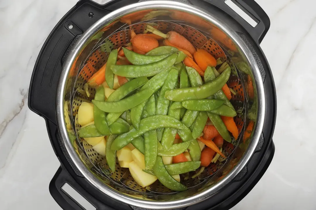 Snow peas, baby carrots, and cubed potatoes in the Instant Pot, about to be steamed