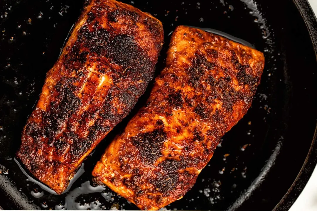 A picture taken from above of two blackened salmon fillets in a black skillet.