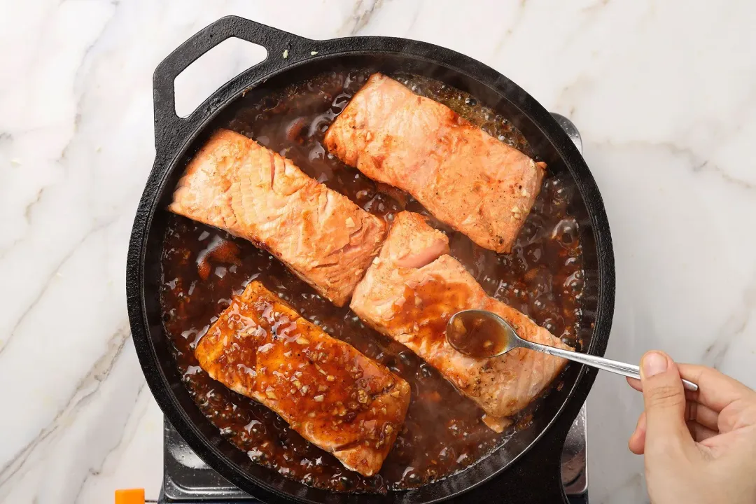 A pan of pan-seared salmon fillets with the pre-mixed sauce being added to the pan