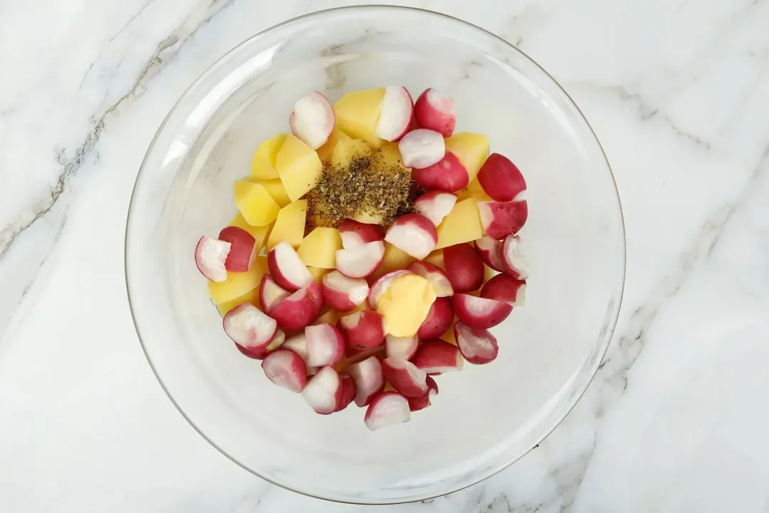 A large glass containing potato cubes and red radish cubes with a pinch of pepper 