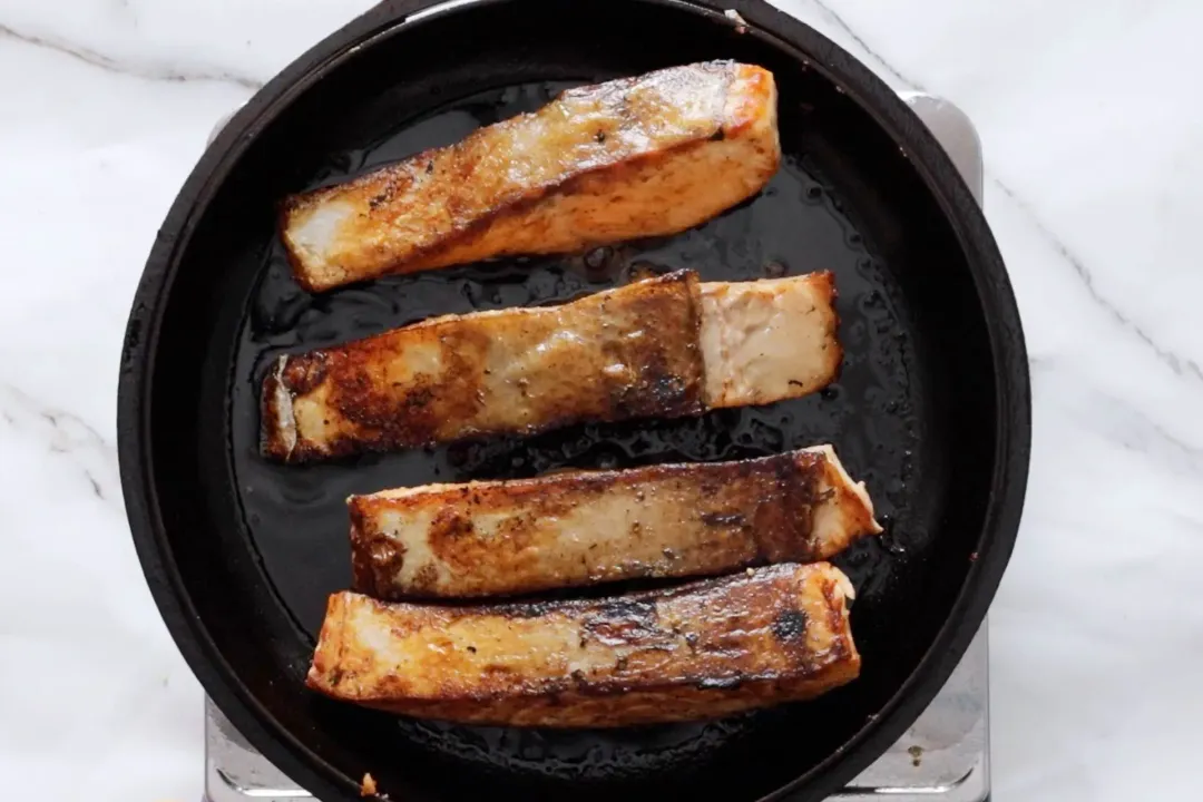 A skillet cooking four salmon fillets with white meat and brown edges
