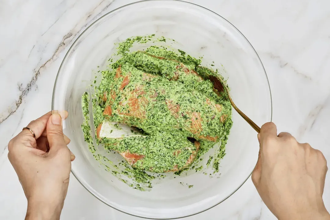 Salmon fillets and a pesto paste in a large glass bowl, about to be mixed