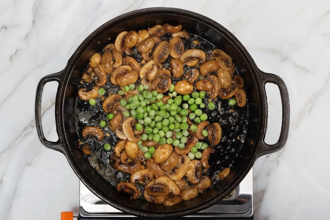 A skillet browning sliced mushrooms and green peas