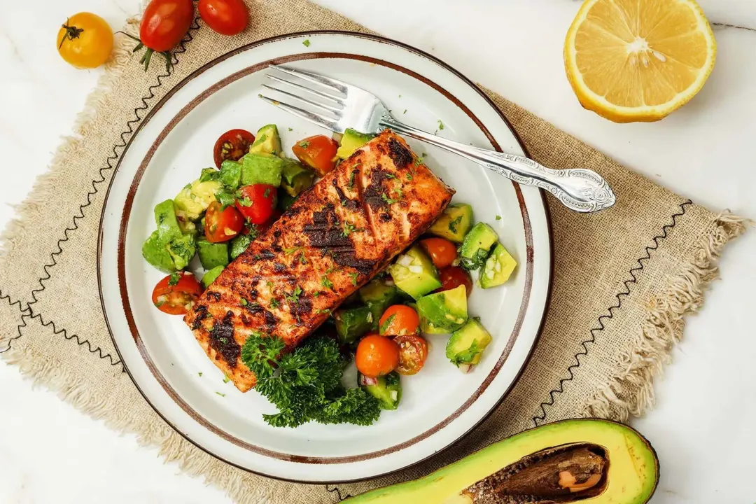 A plate of salmon avocado decorated with a fork, half a lemon, half an avocado and cherry tomatoes