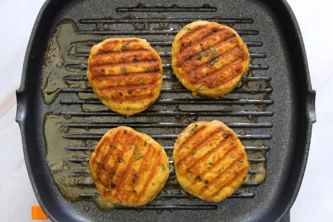 A picture of four salmon croquettes in a black skillet.