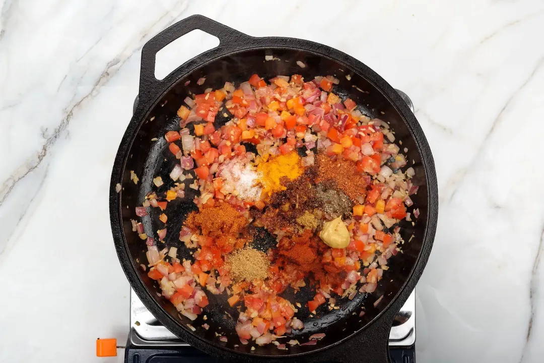 A skillet cooking finely diced vegetables with mustard and various spices