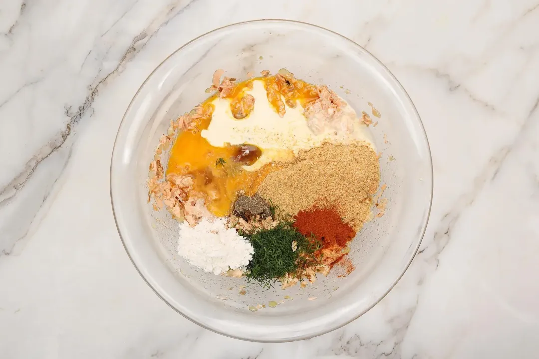 A large glass bowl containing various spices, herbs, egg yolks, and flour