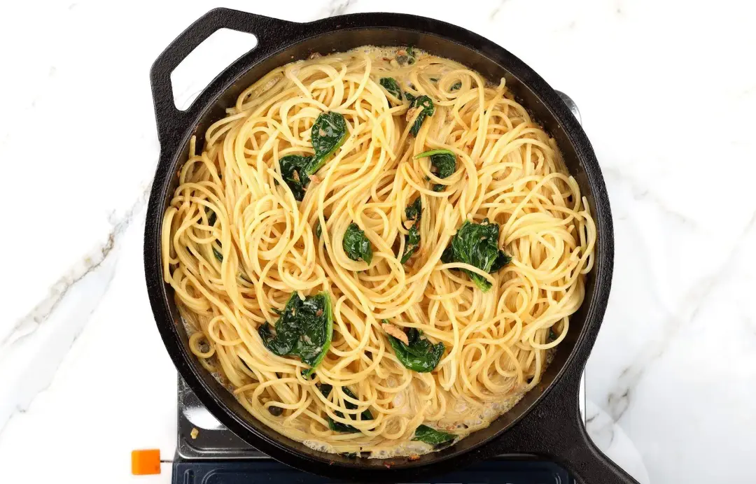 A skillet cooking a lot of spaghetti with several spinach leaves
