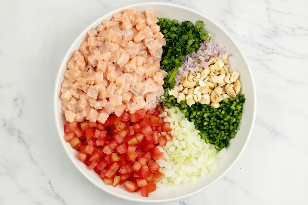 A white platter sectioned with vibrant ingredients: cubed raw salmon, chopped tomatoes, onions, and herbs