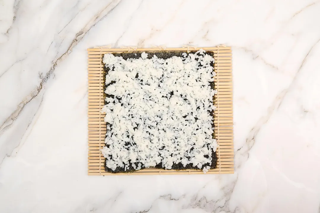 spread rice across seaweed sheet on a bamboo mat