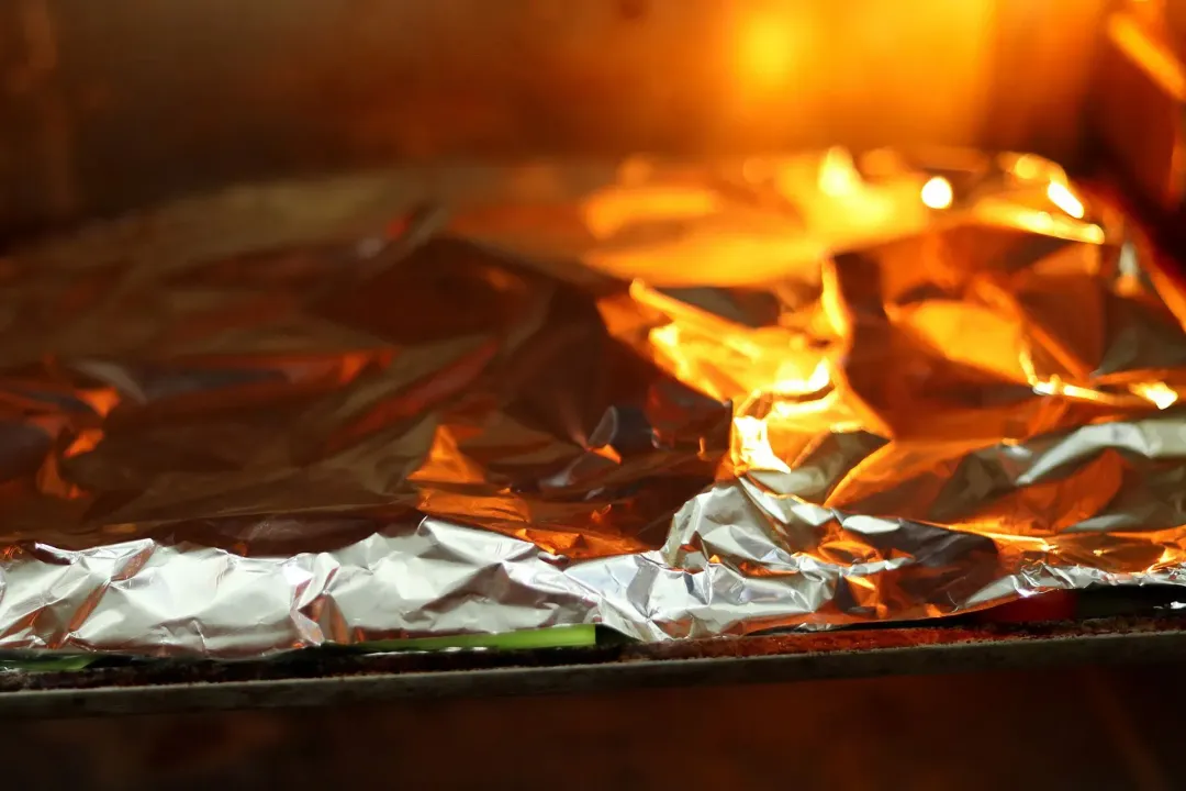 A baking tray of salmon fillets and vegetables covered with aluminium foil in the oven
