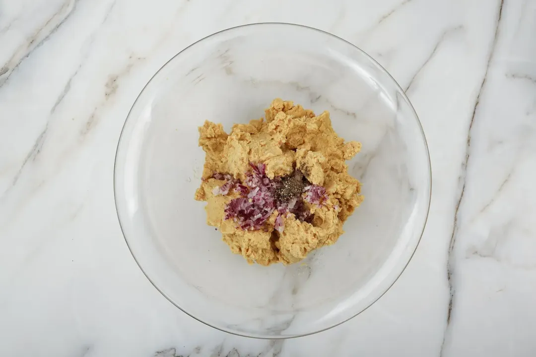 Blended chickpeas, diced red onions, milk, and seasonings in a glass bowl, about to be mixed