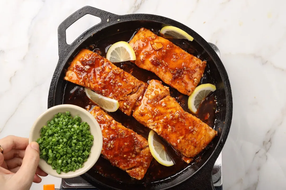 A picture of a pan of honey garlic salmon with some chopped scallions about to be scattered on top of the fish