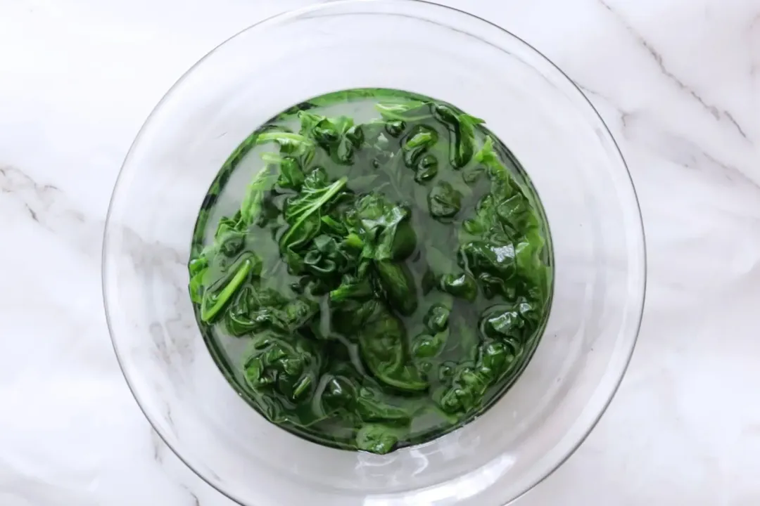 A large glass bowl filled with water and spinach leaves being soaked inside