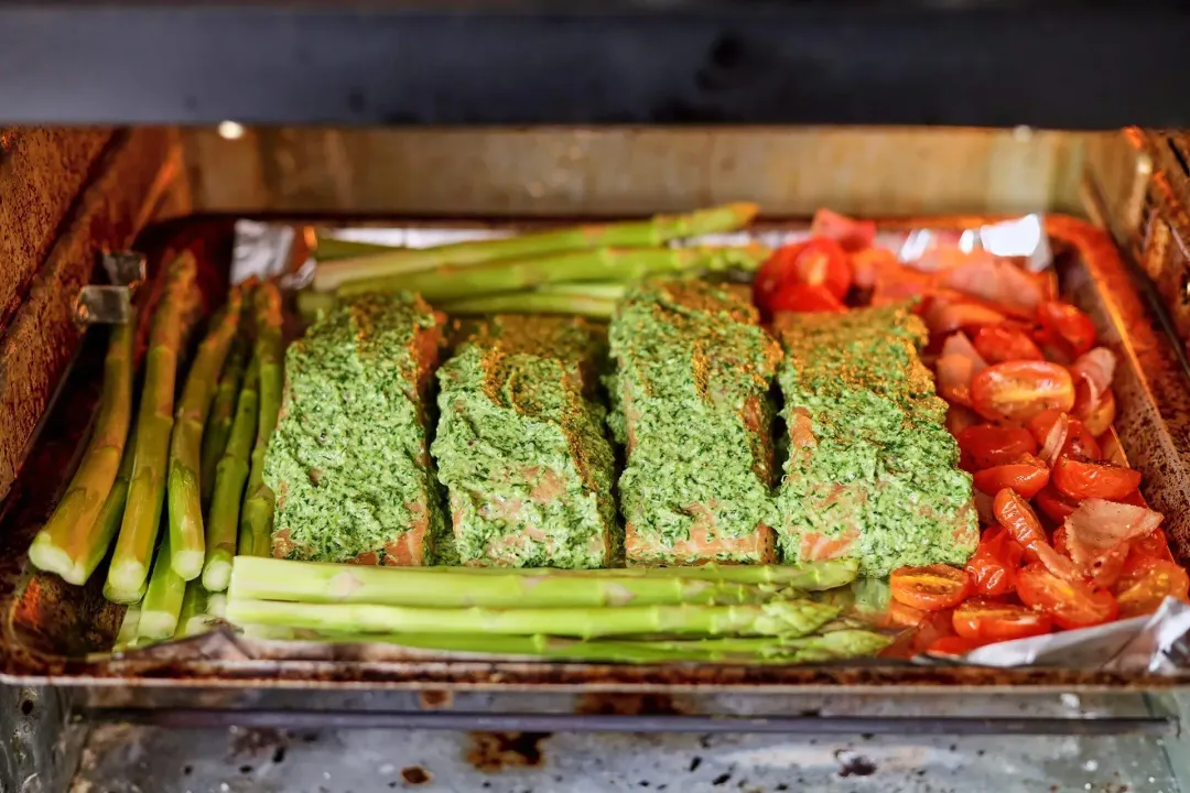 Seasoned salmon fillets, asparagus, halved cherry tomatoes on a baking tray lined with aluminium foil in the oven, ready to be baked