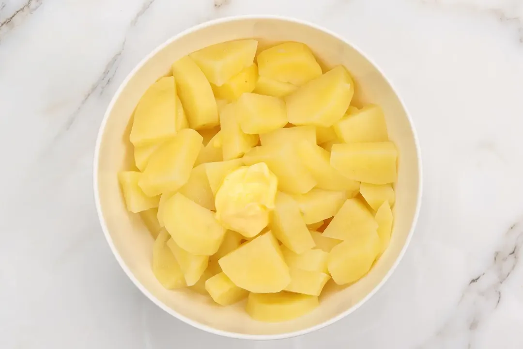 A large white bowl containing large uncooked potato cubes