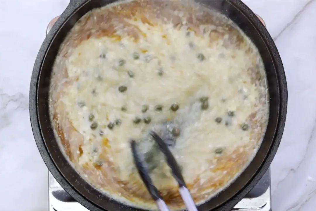 A food grabber is whisking a creamy mixture in a skillet.
