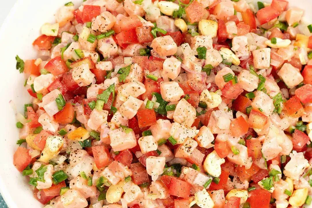 In a white plate a mixture of cubed salmon, tomato, onion, and fresh herbs tossed in dressing