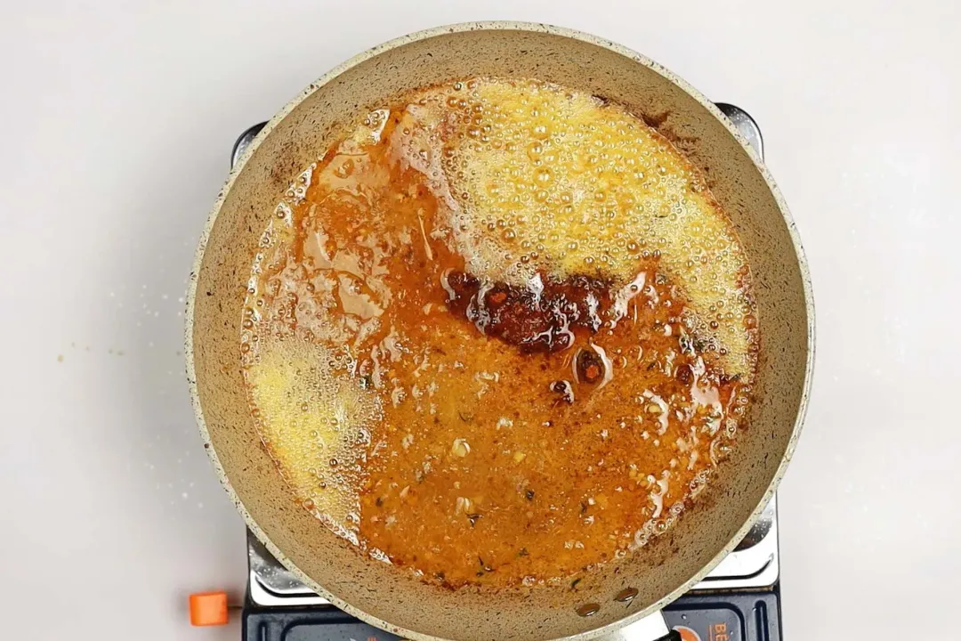 A skillet on a stove with some bubbling oil and seasonings in it.