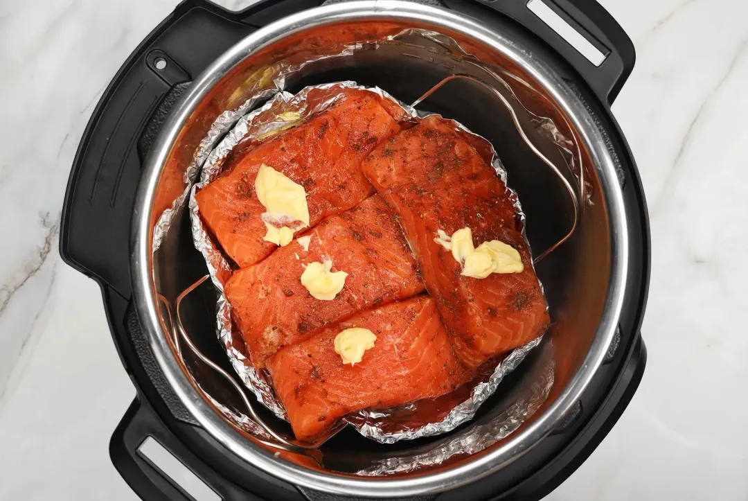 A picture of well-seasoned salmon fillets being add to the foil bowl with some butter in the Instant Pot, about to be cooked