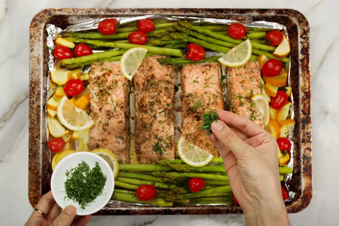 A picture of a completed baked salmon in foil dish with some chopped parsley about to be sprinkled in the dish