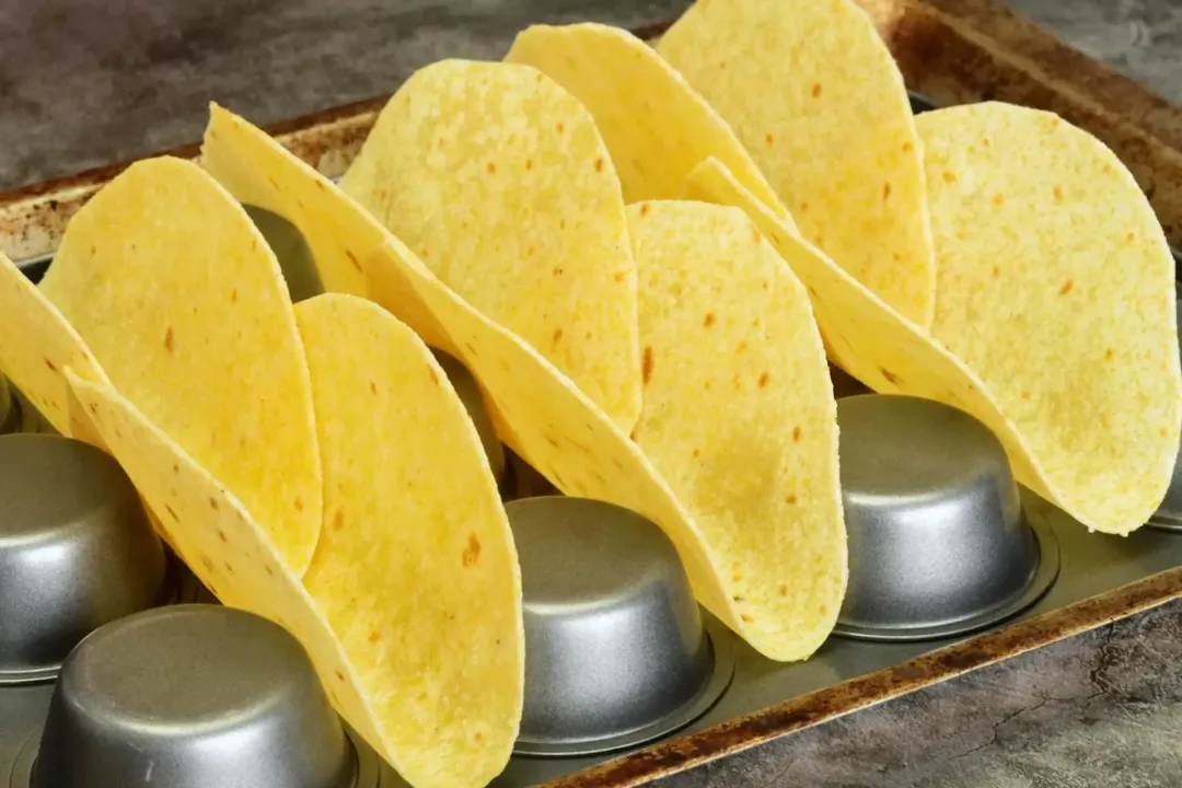 A picture of six yellow corn tortillas placed between the cupcake trays.