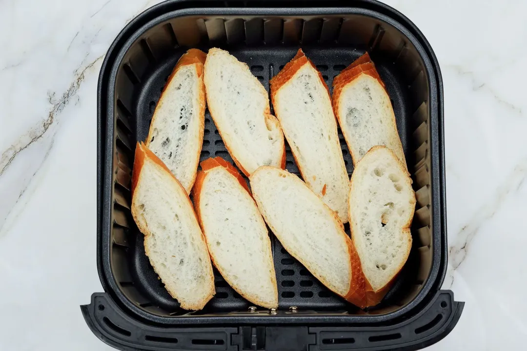 Slices of baguette in the air-fryer basket, about to be air-fried
