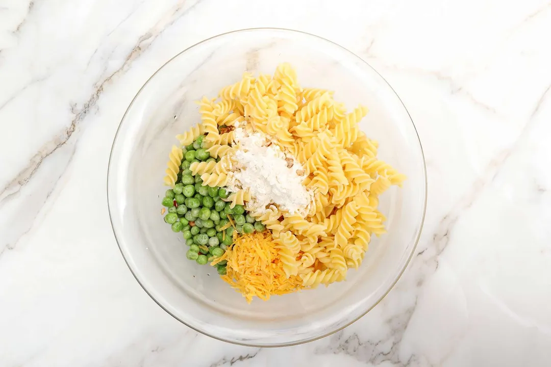 fusilli pasta, green peas, flour and cheese in a glass bowl