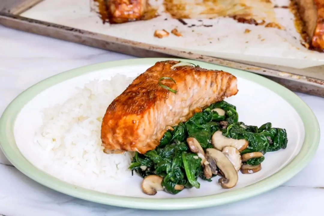 A plate containing white rice, a piece of cooked salmon fillet, cooked spinach, and cooked mushroom