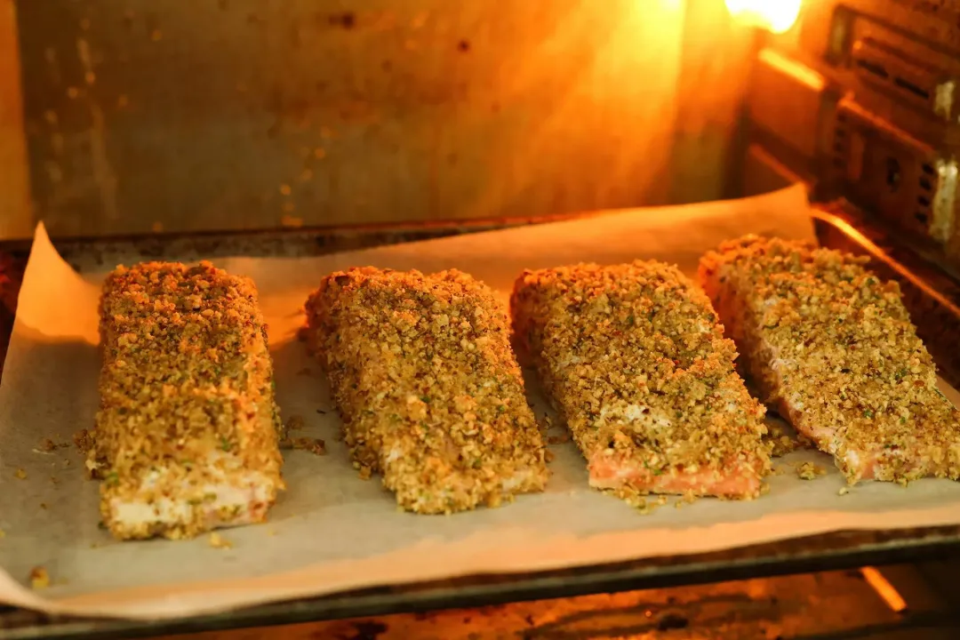 Four fully crust-coated salmon filets are being put in an oven for baking.