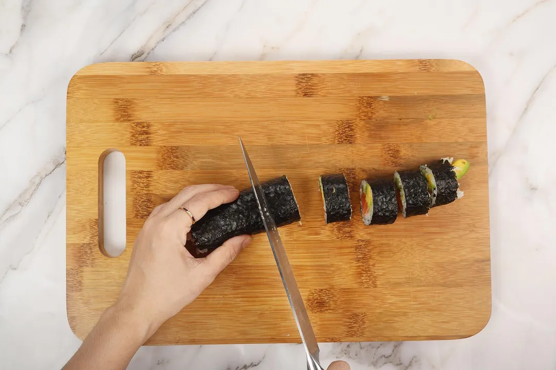 cutting a sushi roll into pieces on a cutting board