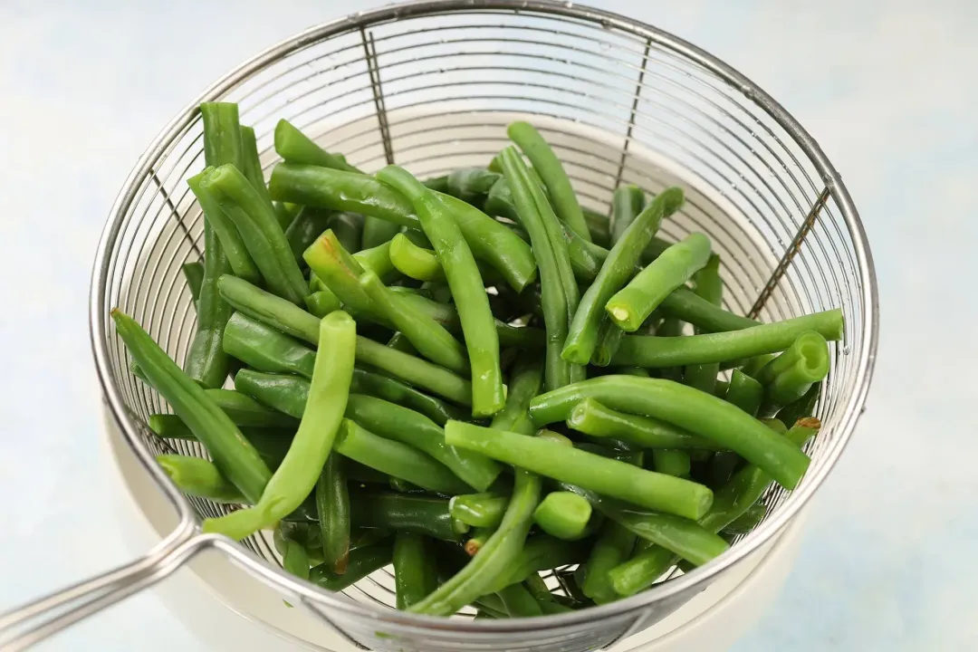 Microwaved green beans are placed in a strainer set over a large bowl to drain off excess water.