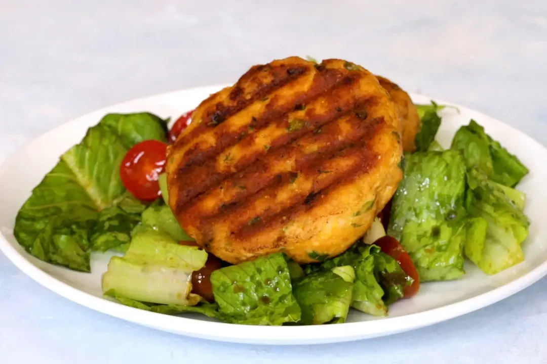 A picture of salmon croquettes on a bed of green lettuce and some tomatoes on a white plate.