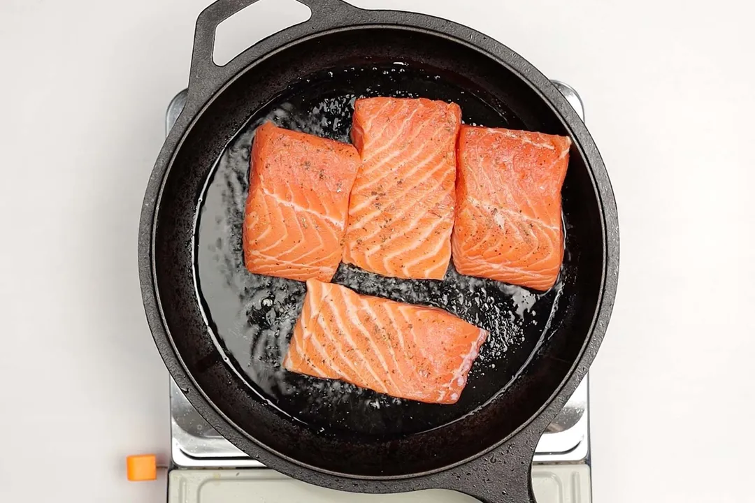four salmon fillet cooking in a cast iron skillet