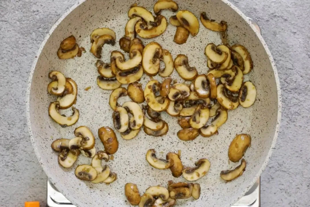 A large pan cooking and browning a bunch of sliced cremini mushrooms