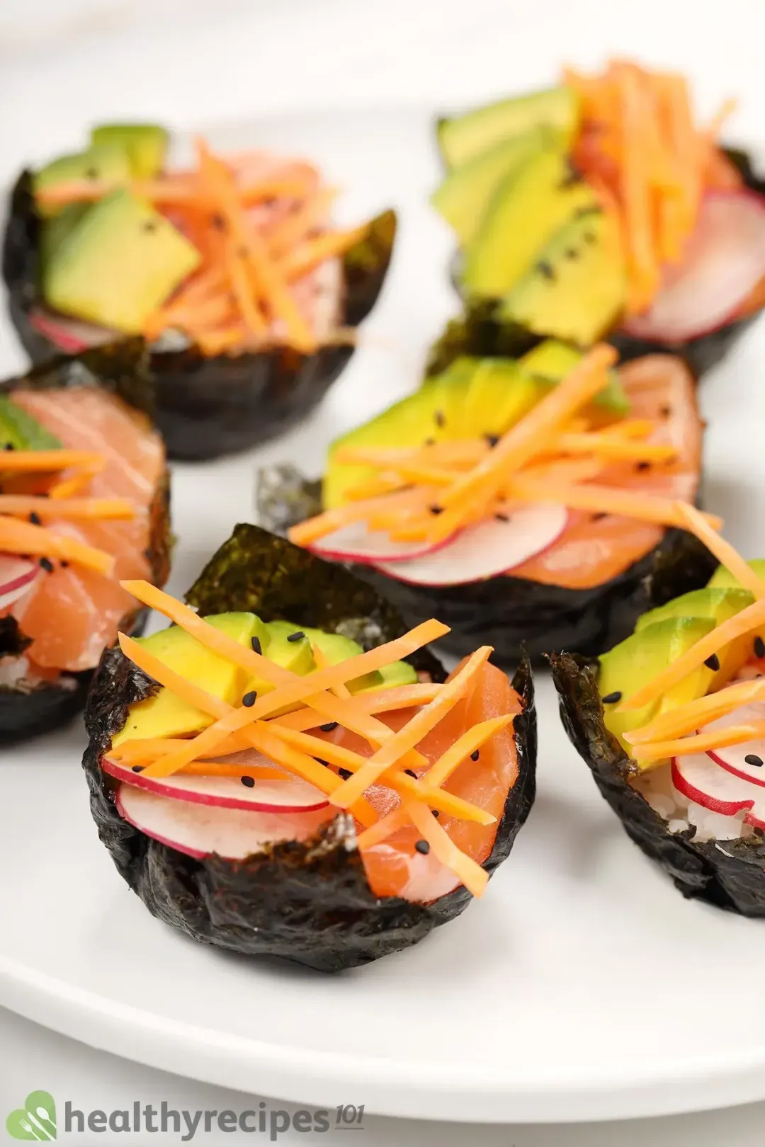 Six sushi cups of nori, sliced carrots, avocado cubes, pink radish, and salmon