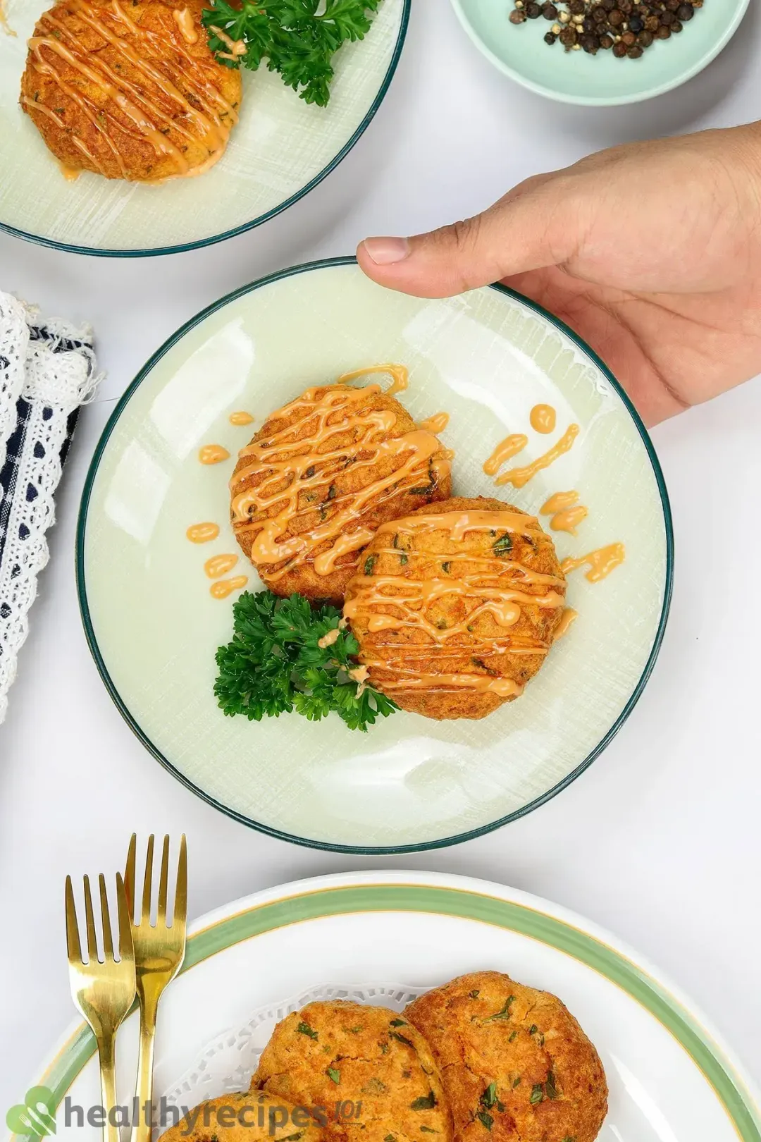 A hand holding a plate of two air fryer salmon patties drizzled with sauce and garnished with some parsley.