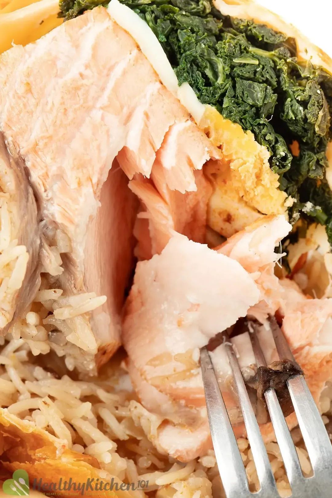 A fork slicing into a piece of cooked salmon, surrounded by rice, eggs, and cooked kale