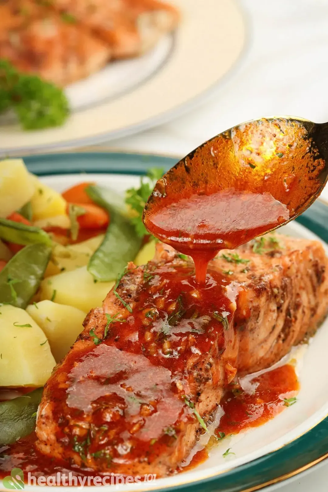 A close-up picture of Instant Pot salmon drizzled with a spicy sauce and served with some cooked vegetables on the side