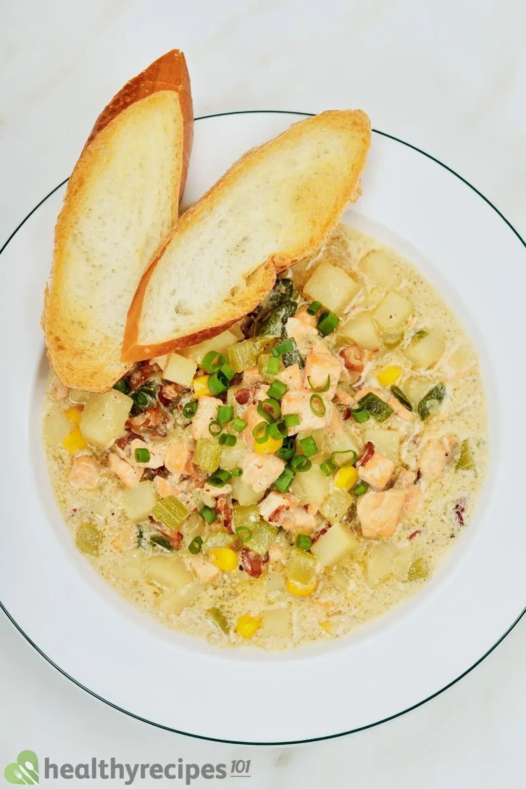 A picture of a plate of salmon chowder with two slices of baguette taken from above