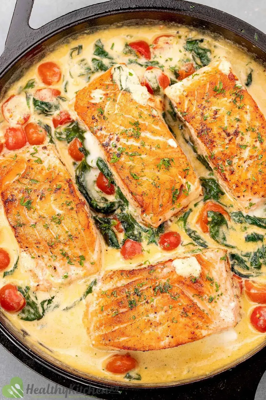 Four golden salmon filets swimming in a cream sauce cooked with cherry tomatoes and spinach