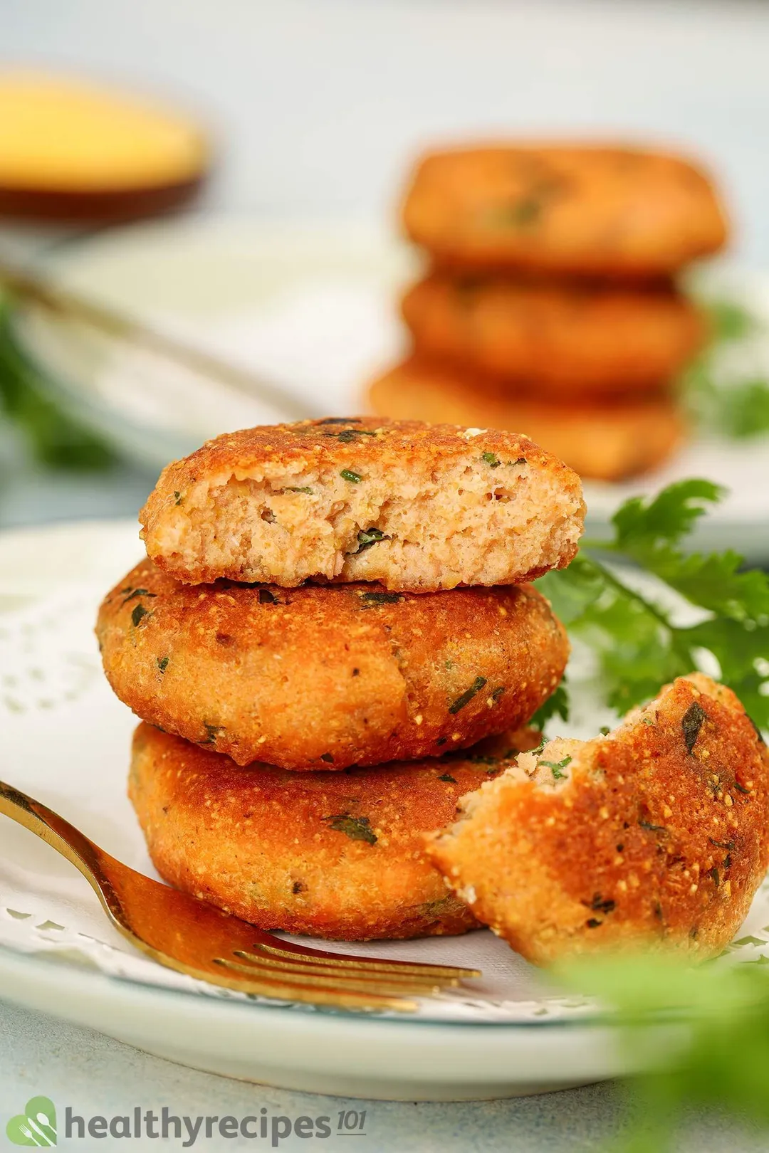 three salmon patties on a plate garnished with a golden fork and coriander