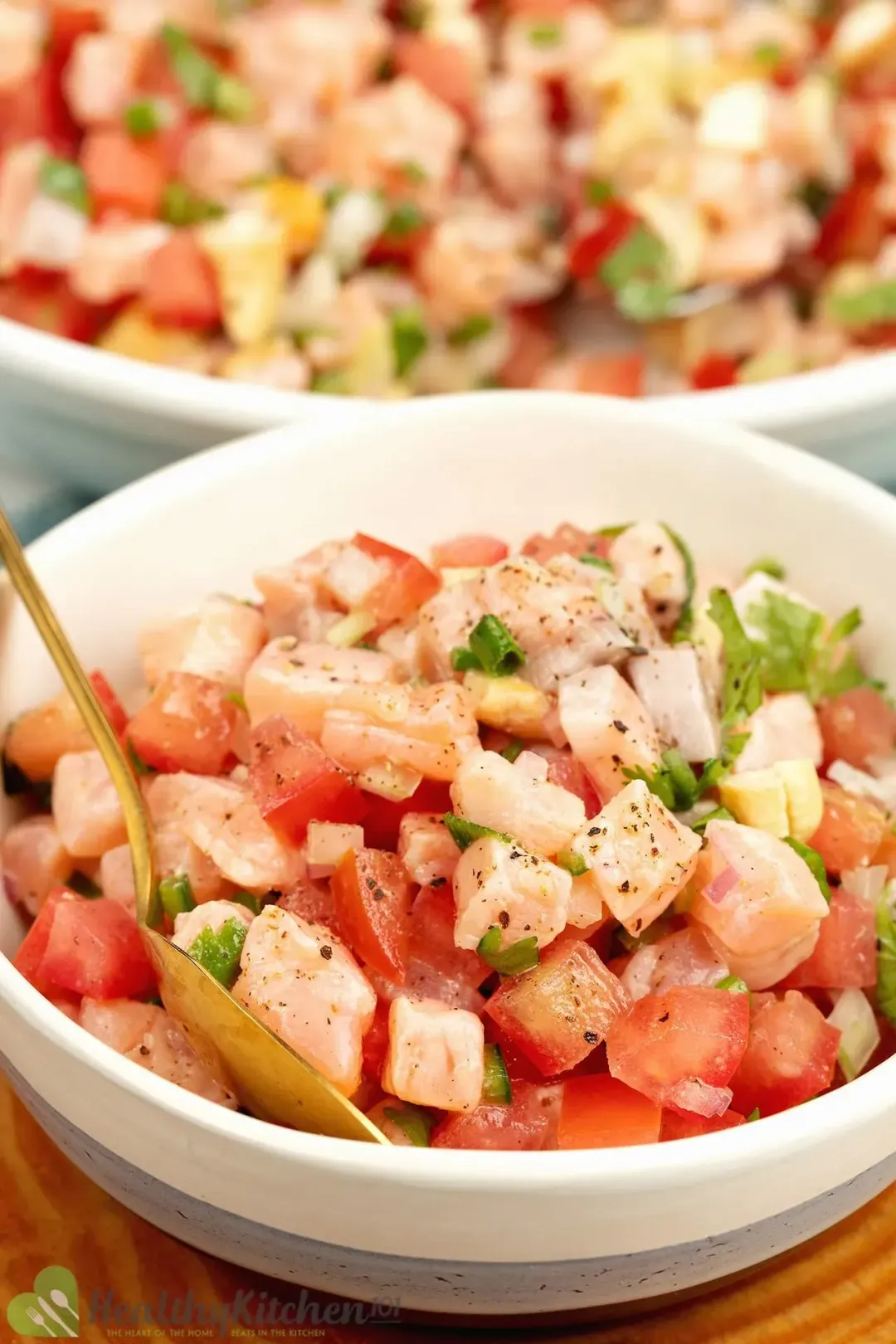 A bowl of cubed salmon, tomatoes, and chopped cilantro mixed in a white bowl underneath a larger plate of salmon Lomi Lomi