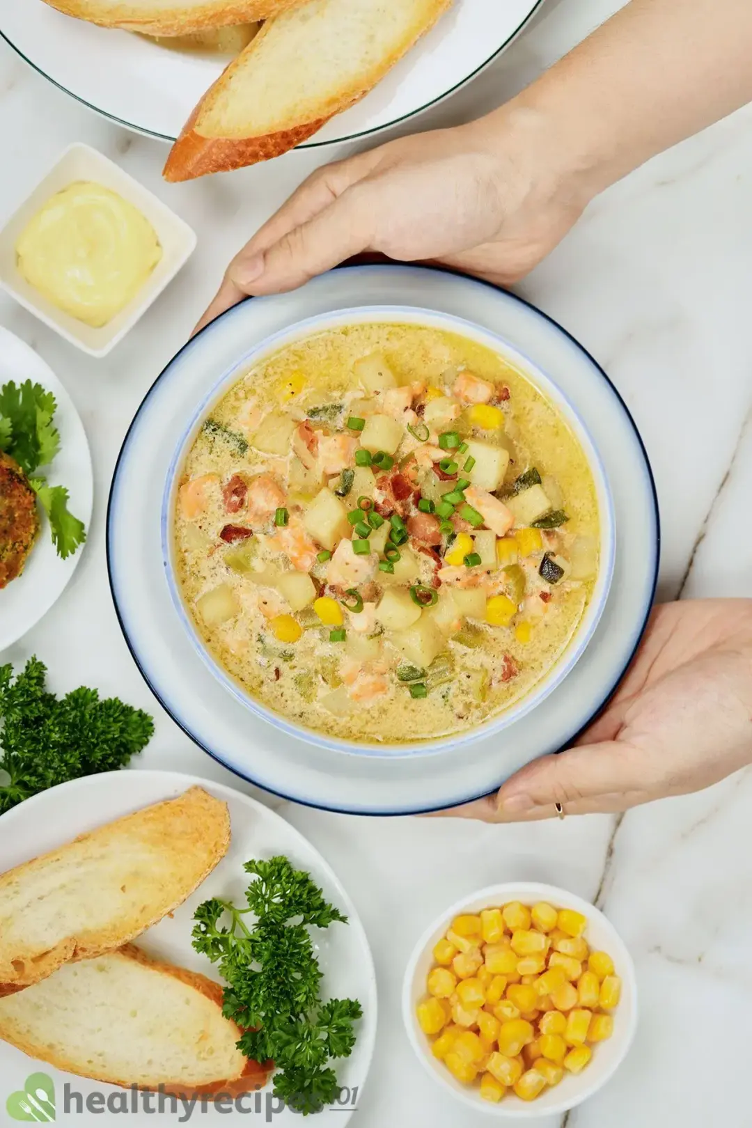 A large bowl of salmon chowder surrounded with some air-fried baguette slices and canned corn
