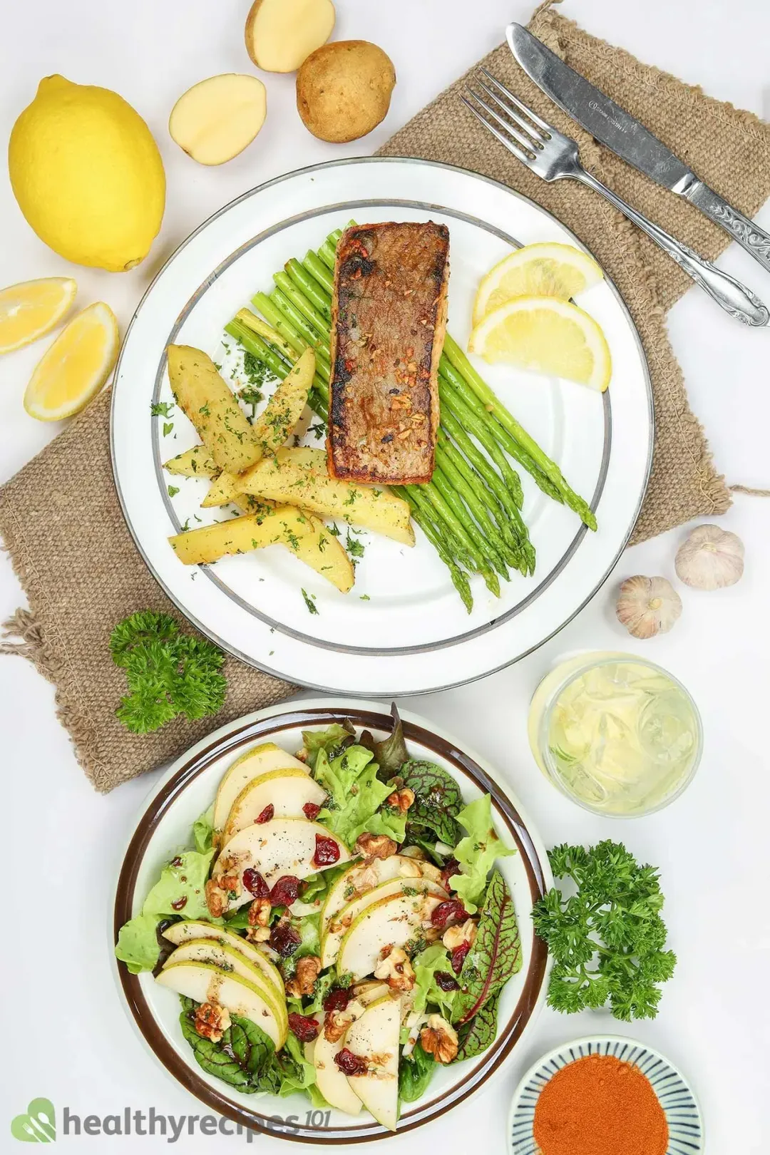 A flatlay of a lemon, lemon slices, potatoes, a pear salad, and a plate holding a salmon fillet, asparagus, potato wedges, and two lemon slices
